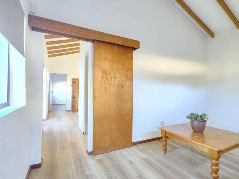 A bright living area featuring exposed timber ceiling beams, laminate flooring, and a large sliding timber door leading to the hallway.