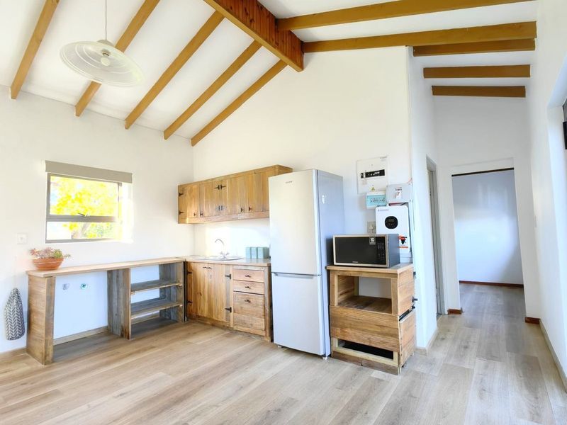 A rustic-style kitchen featuring exposed timber ceiling beams, wooden cabinetry, laminate flooring, and a functional layout with integrated shelving and sink area.