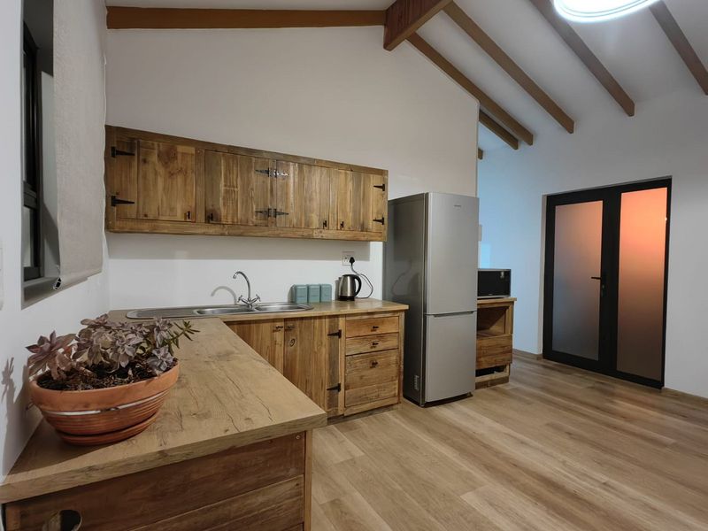 A rustic-style kitchen featuring wooden cabinetry, exposed timber ceiling beams, and modern laminate flooring, creating a warm and functional cooking space.