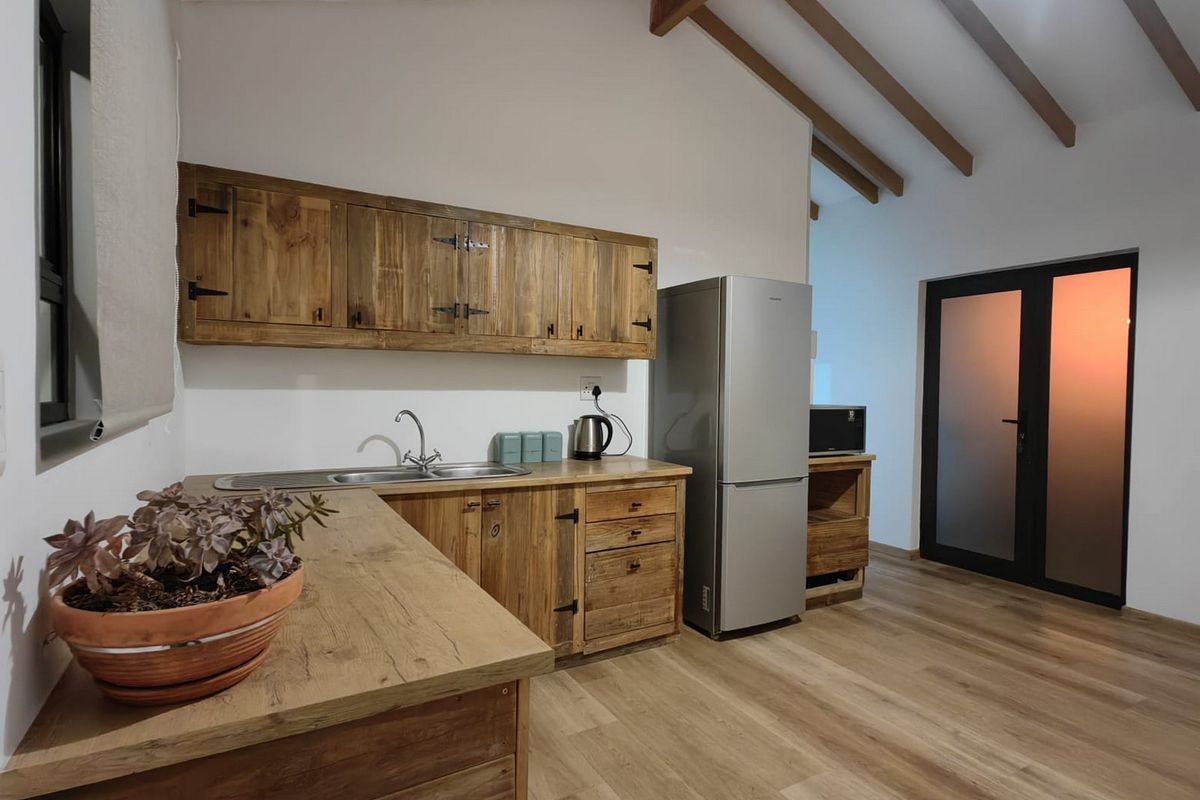 A rustic-style kitchen featuring wooden cabinetry, exposed timber ceiling beams, and modern laminate flooring, creating a warm and functional cooking space.