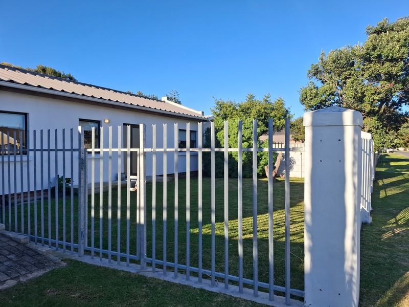 Front view of the property featuring a secure metal palisade fence, concrete pillar, and a well-maintained lawn area leading to the house entrance.