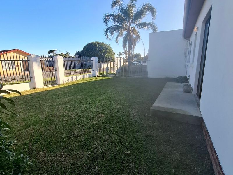 A private rear garden featuring a well-maintained lawn, concrete patio area, and secure metal perimeter fencing.