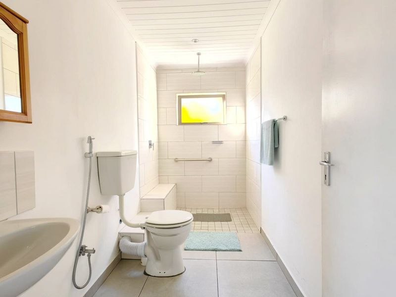 A functional bathroom featuring a walk-in shower with grab rail, wall-mounted basin, and neutral tiled finishes throughout.