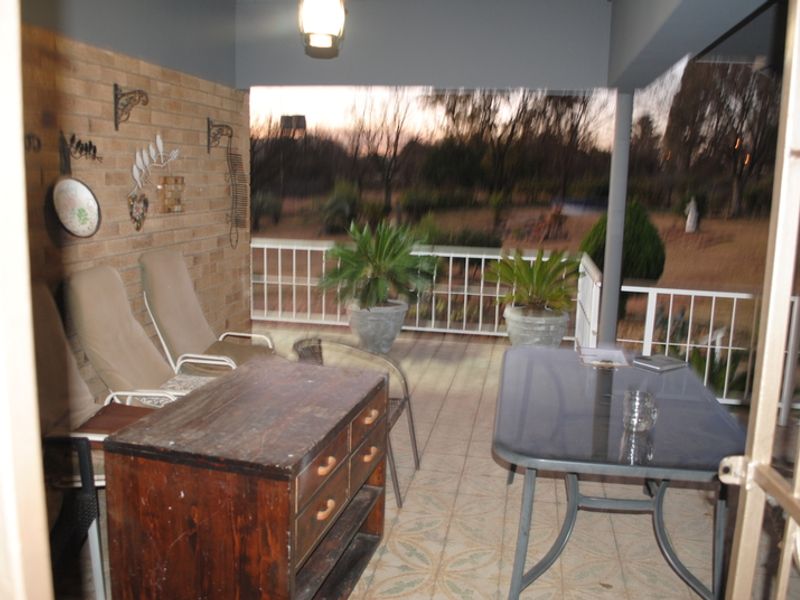 A covered patio area featuring a brick wall, tiled flooring, and a metal balustrade overlooking the garden.