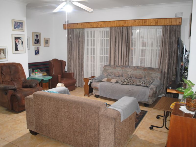 A spacious living room featuring tiled flooring, a ceiling fan, and large sliding glass doors with a wooden pelmet finish.