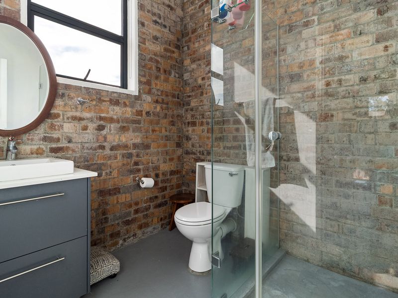 Modern industrial-style bathroom featuring exposed brick walls, a glass-enclosed shower, a sleek vanity with a vessel sink, and polished concrete flooring.