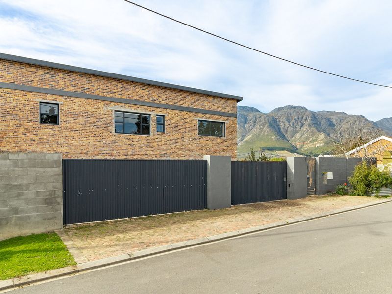 Street view of a modern face brick house featuring a secure corrugated metal gate, concrete boundary walls, and mountain views in the background.