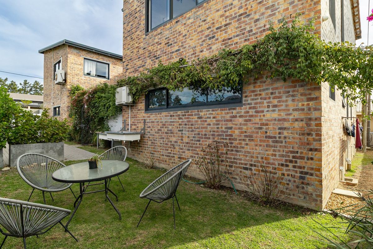 A rear garden area featuring a face brick exterior wall, aluminium window frames, and an external utility sink.