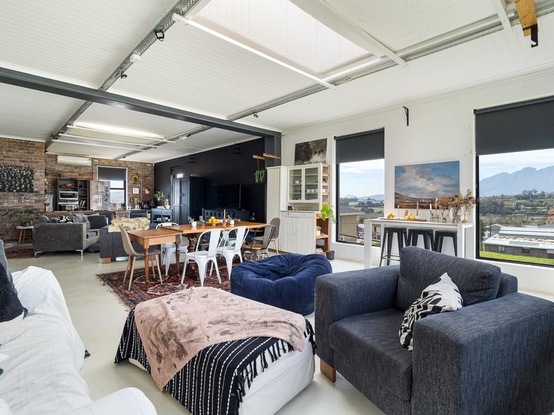 Spacious open-plan living area featuring industrial-style exposed steel beams, a large skylight, polished concrete floors, and expansive windows with scenic mountain views.