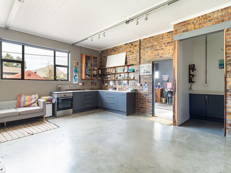 Industrial-style kitchen featuring exposed brick walls, polished concrete floors, modern grey cabinetry, and an integrated oven, with an adjacent utility area.