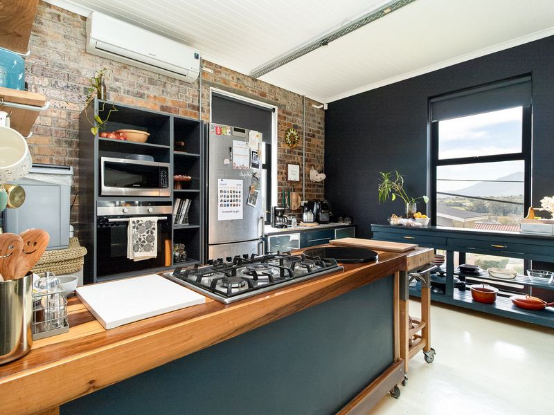 Modern industrial-style kitchen featuring exposed brick walls, a timber-topped island with a gas cooktop, built-in appliances, and a split system air conditioner.