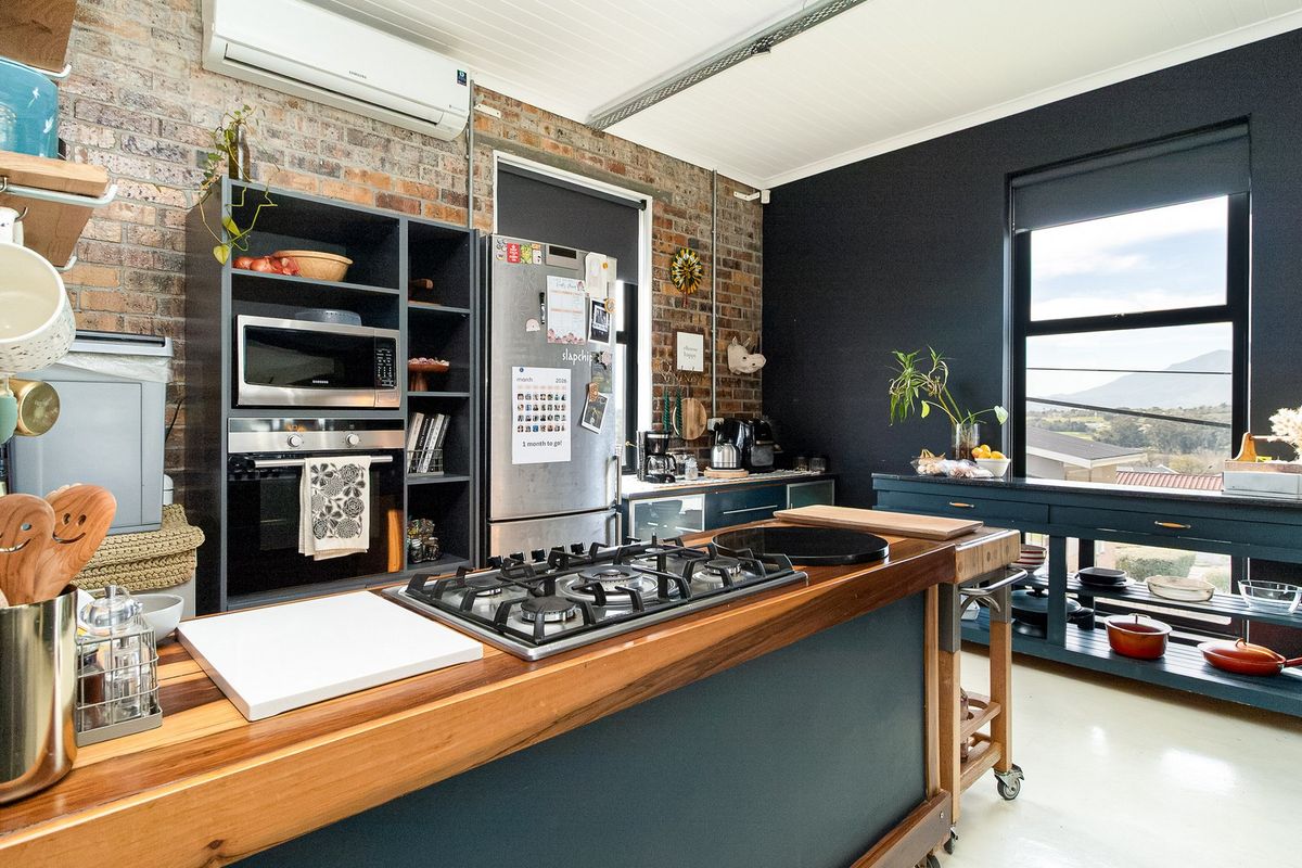 Modern industrial-style kitchen featuring exposed brick walls, a timber-topped island with a gas cooktop, built-in appliances, and a split system air conditioner.