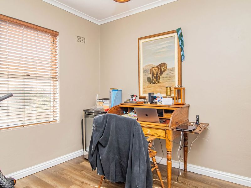 A functional home office space featuring laminate flooring, built-in wardrobe storage, and natural light through venetian blinds.