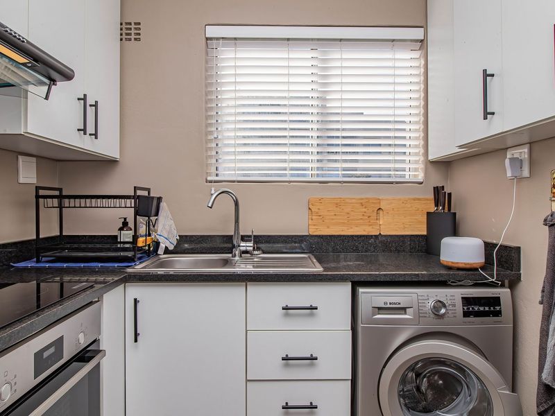 A well-maintained kitchen featuring modern white cabinetry, dark granite countertops, built-in oven, hob, extractor fan, and a dedicated space for a washing machine.