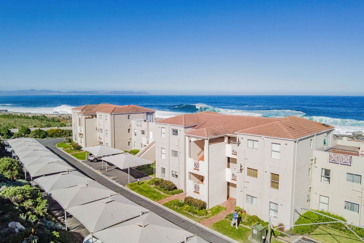 Aerial view of a coastal apartment complex featuring tiled roofs, covered parking bays, and well-maintained grounds overlooking the ocean.