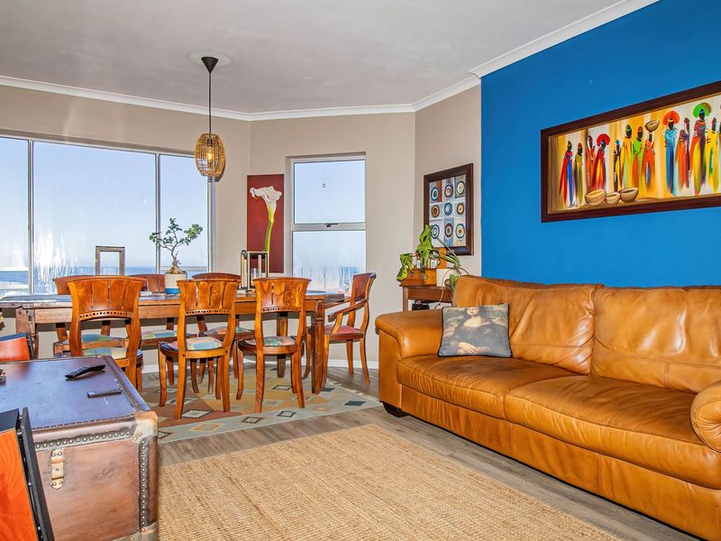 Spacious open-plan living and dining area featuring large windows with natural light, laminate flooring, and a vibrant blue accent wall.