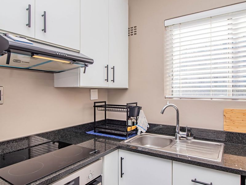 Modern kitchen featuring granite countertops, stainless steel sink, built-in oven, electric hob, extractor fan, and ample cabinetry with venetian blinds.