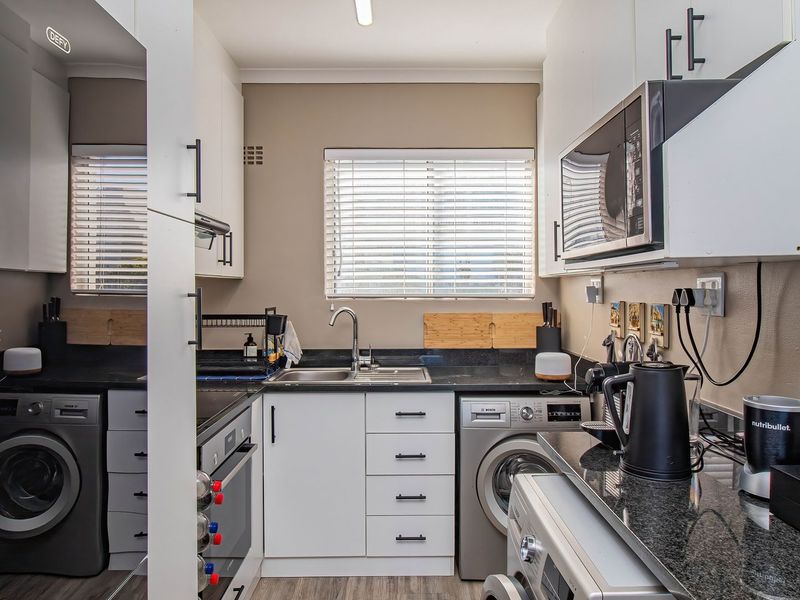 Compact, well-organized kitchen featuring modern white cabinetry, granite countertops, built-in appliances, and integrated laundry facilities, maximizing space efficiency.