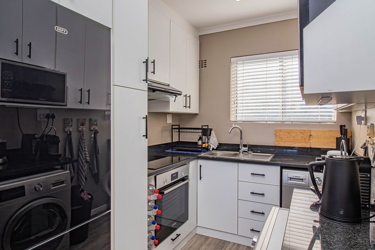 Modern kitchen featuring granite countertops, built-in oven, hob, extractor fan, integrated dishwasher, and ample cabinetry with a clean, functional layout.