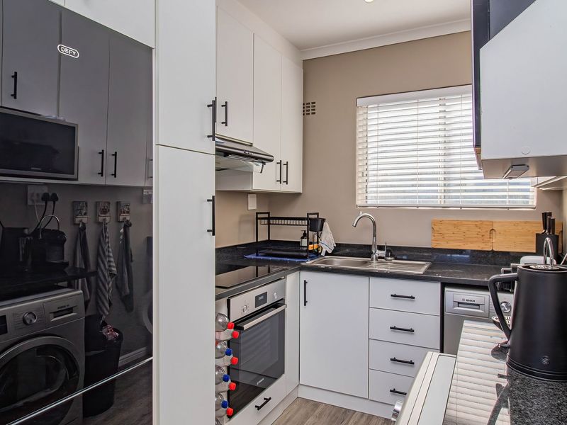Modern kitchen featuring granite countertops, built-in oven, hob, extractor fan, integrated dishwasher, and ample cabinetry with a clean, functional layout.