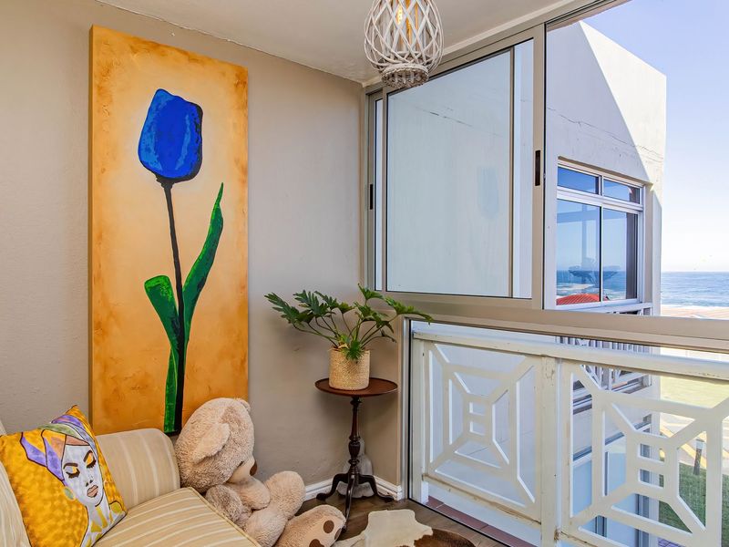 A bright enclosed balcony area featuring large sliding windows, a decorative balustrade, and a pleasant coastal view.