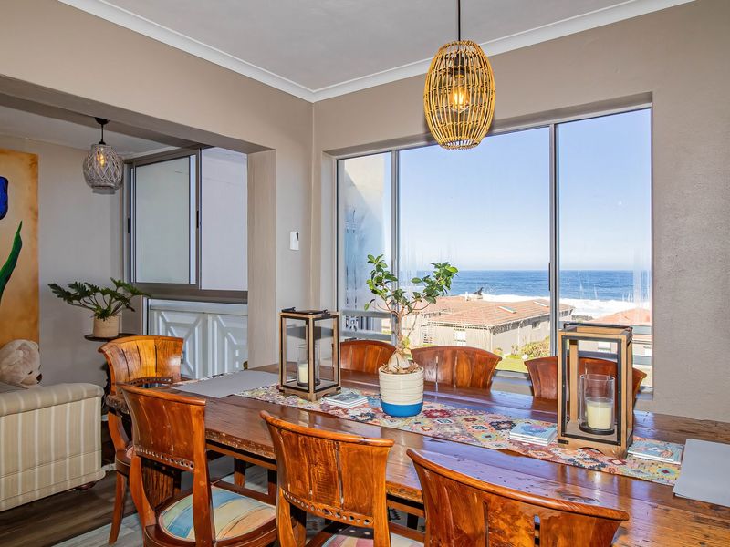 Dining area featuring large sliding glass doors with ocean views, neutral wall tones, and decorative pendant lighting.