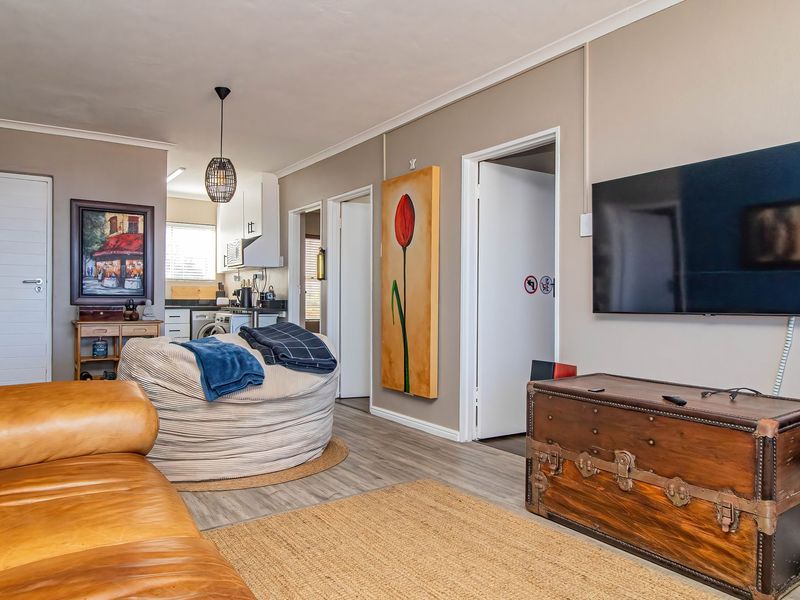An open-plan living area featuring laminate flooring, neutral wall tones, and a seamless transition into the adjacent kitchen space.