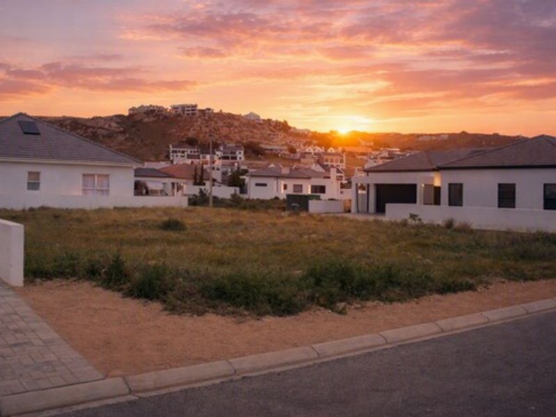 A vacant residential plot situated in a developed neighborhood, featuring a paved sidewalk and boundary wall, captured during a scenic sunset.