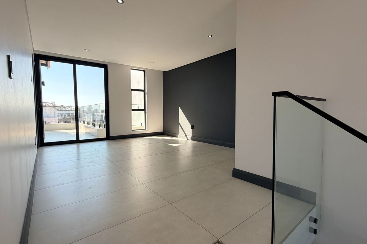 A bright, modern, and empty living area featuring large format floor tiles, recessed lighting, and a glass balustrade leading to an outdoor balcony.