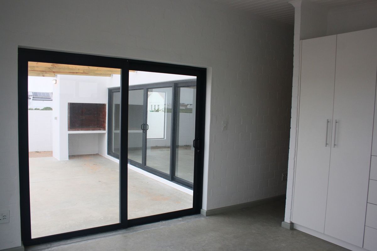 Bright living area featuring polished concrete floors, built-in storage, and large sliding doors opening onto a covered patio with a built-in braai.