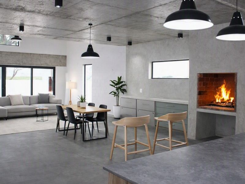 Spacious open-plan living area featuring an exposed concrete ceiling, polished concrete floors, a built-in fireplace, and modern pendant lighting throughout.