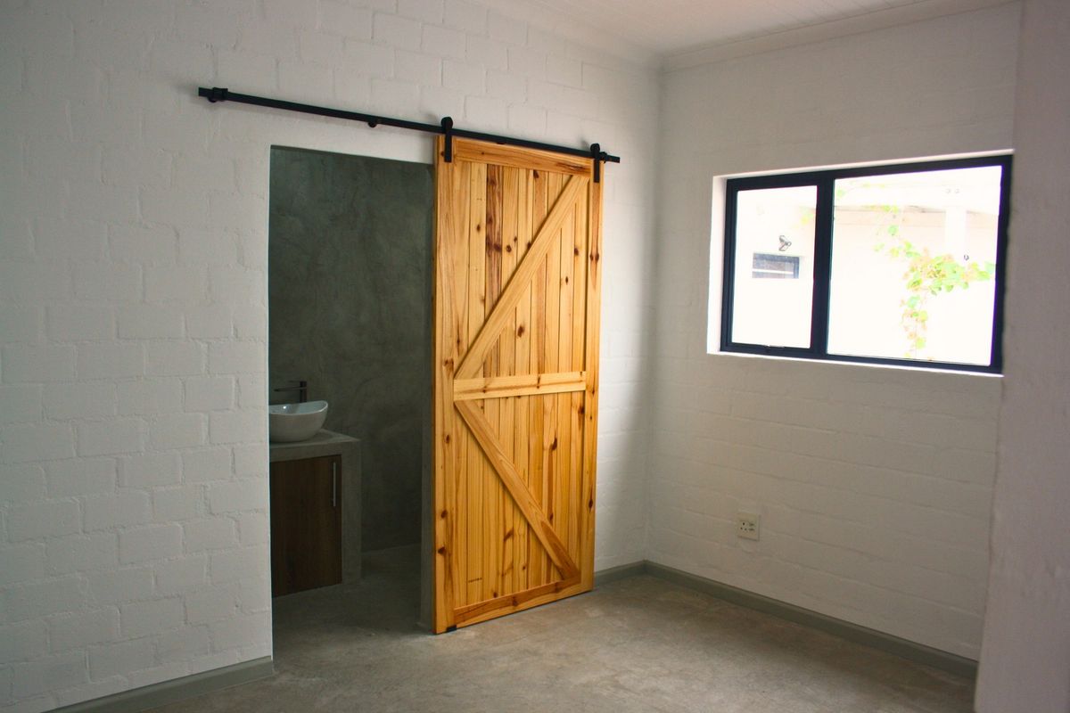 A minimalist bedroom featuring painted brick walls, polished concrete flooring, and a rustic wooden sliding barn door leading to an en-suite bathroom.