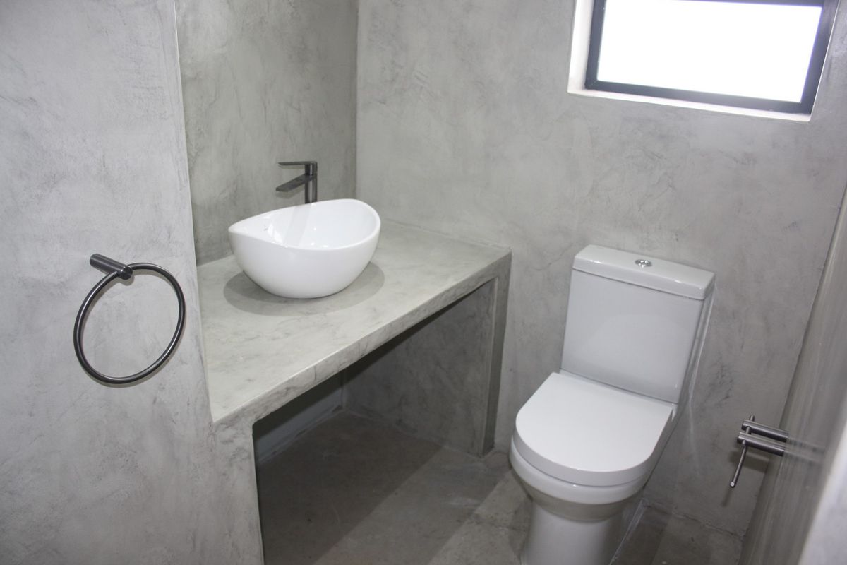 Modern bathroom featuring a concrete vanity with a vessel sink, dual flush toilet, and polished concrete wall finishes.