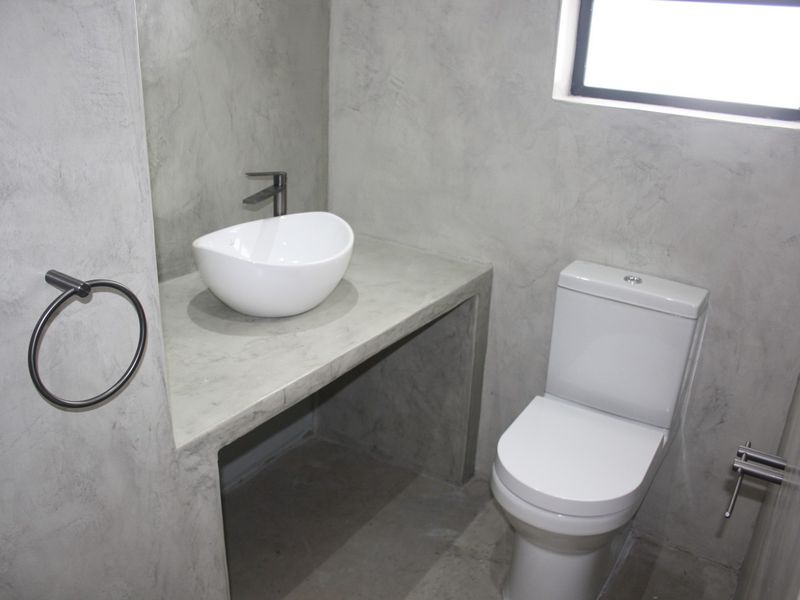 Modern bathroom featuring a concrete vanity with a vessel sink, dual flush toilet, and polished concrete wall finishes.