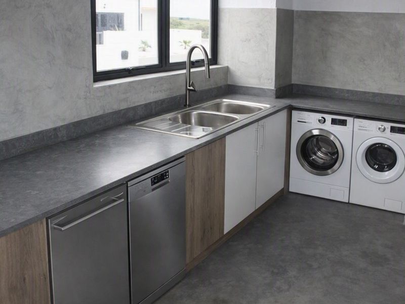 Modern laundry room featuring sleek grey cabinetry, stone-look countertops, a double stainless steel sink, and integrated appliance spaces.