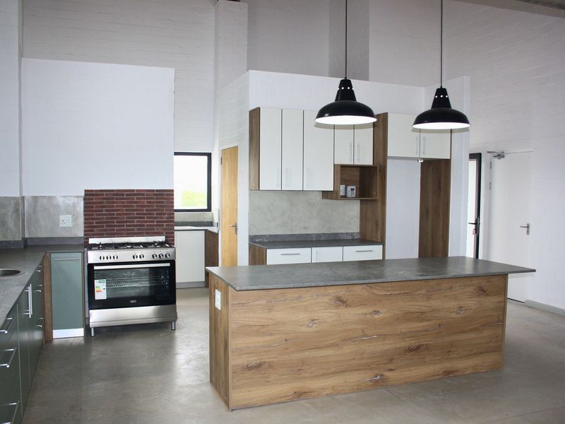 Modern kitchen featuring a central island, built-in gas oven, sleek cabinetry, and polished concrete floors in an open-plan industrial-style space.