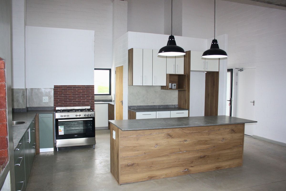 Modern kitchen featuring a central island, built-in gas oven, sleek cabinetry, and polished concrete floors in an open-plan industrial-style space.