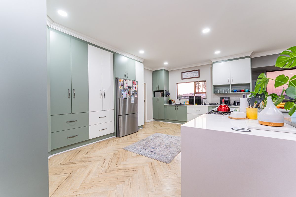 Modern kitchen featuring two-tone cabinetry, a central island with stone countertops, and stylish herringbone flooring, complemented by recessed lighting.