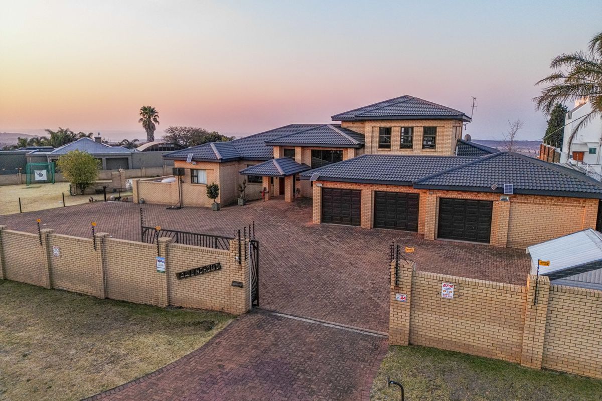 Aerial view of a large residential property featuring a triple garage, extensive paved driveway, and secure perimeter walling with electric fencing.