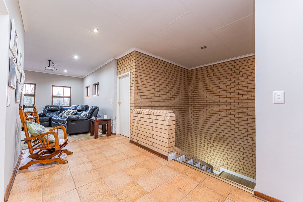 A living area featuring exposed brick walls, tiled flooring, and an open staircase leading to the lower level.