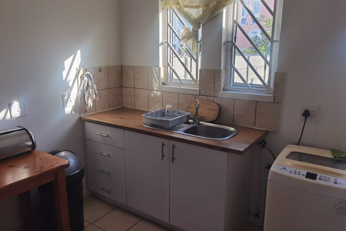 A functional kitchen area featuring a stainless steel sink, tiled backsplash, laminate countertops, and built-in cabinetry with security bars on the windows.