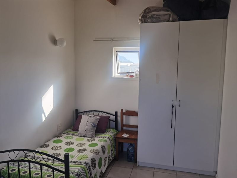 A compact bedroom featuring tiled flooring, a built-in wardrobe, and a top-hung window providing natural light.