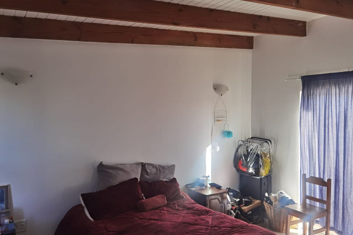A bedroom featuring exposed timber ceiling beams, wall-mounted lighting, and a sliding glass door providing access to the exterior.