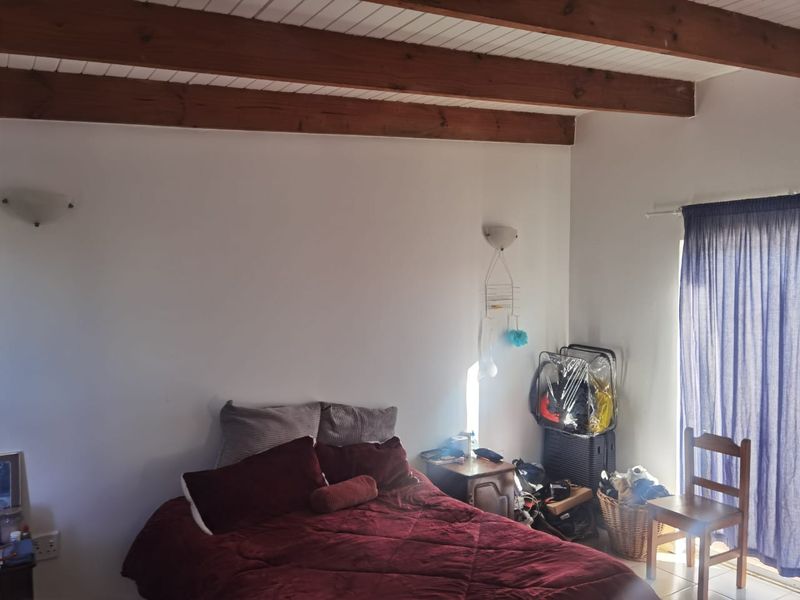 A bedroom featuring exposed timber ceiling beams, wall-mounted lighting, and a sliding glass door providing access to the exterior.