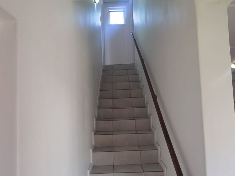 A simple interior staircase featuring tiled steps and a wooden handrail, leading to an upper level with a small window.