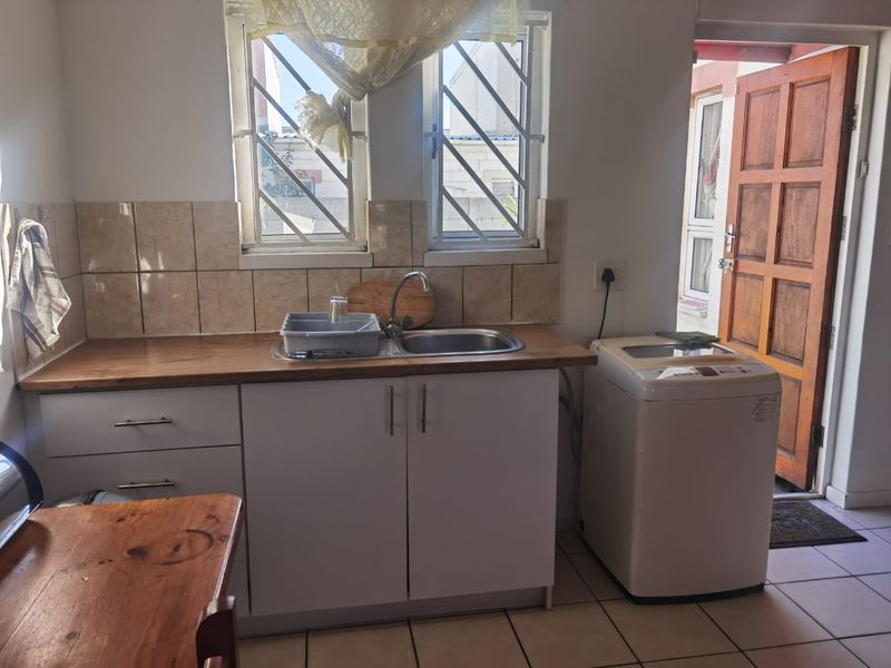 Functional laundry area featuring built-in cabinetry, a stainless steel sink, tiled backsplash, and direct access to the exterior.