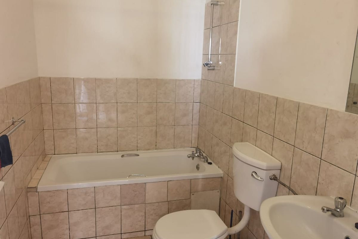 A functional bathroom featuring a bathtub with shower attachment, pedestal basin, and toilet, finished with neutral ceramic wall and floor tiling.