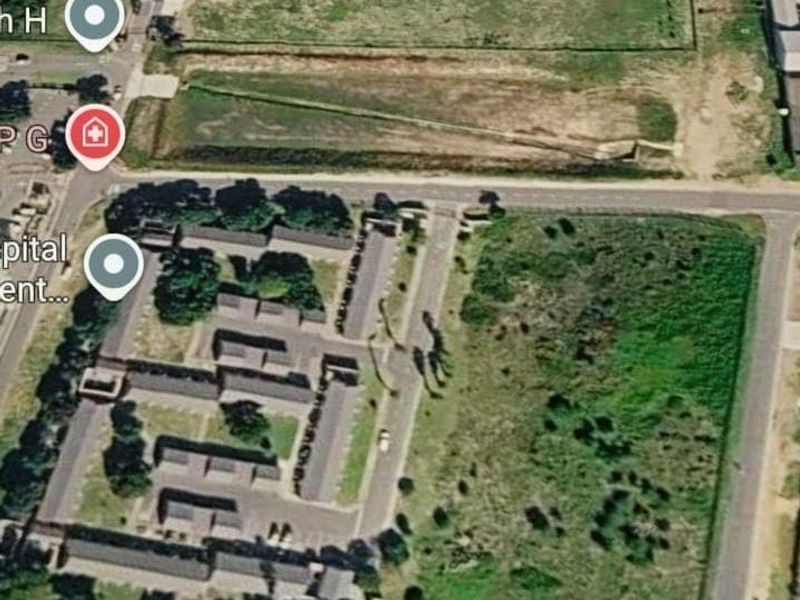 An aerial view of a vacant residential land parcel situated near existing residential developments and road infrastructure.