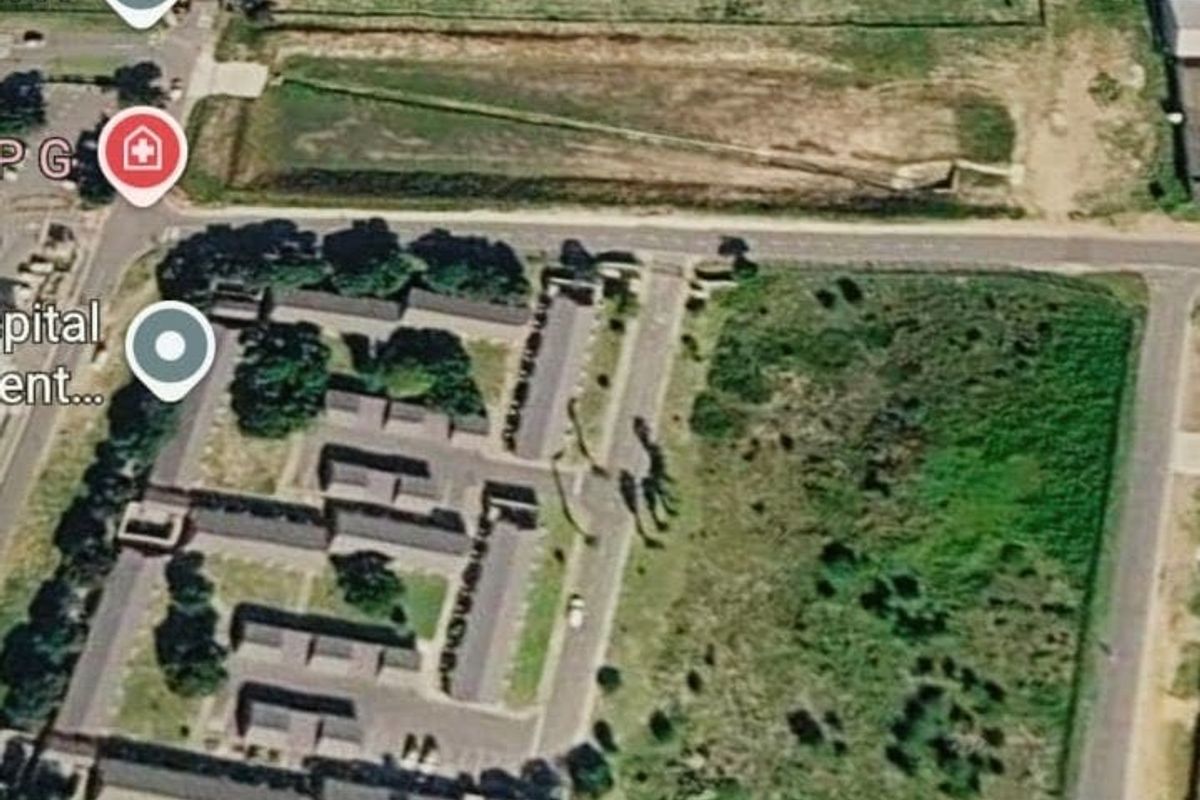 An aerial view of a vacant residential land parcel situated near existing residential developments and road infrastructure.