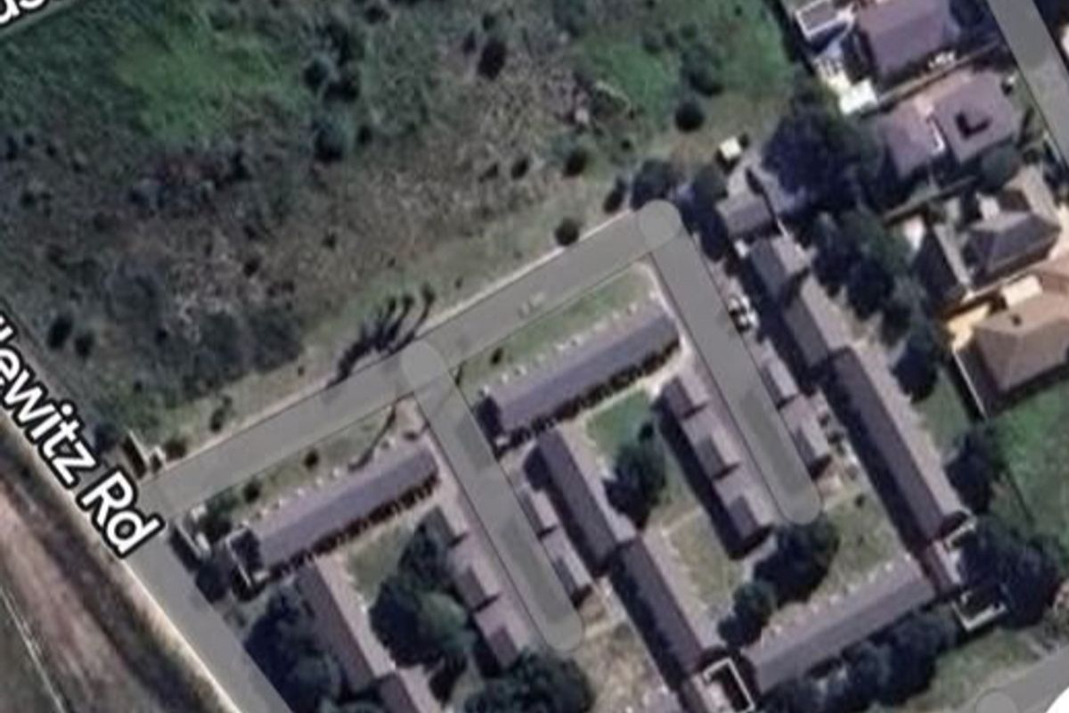 Aerial view of a residential complex and adjacent vacant land parcel situated at the intersection of local roads.